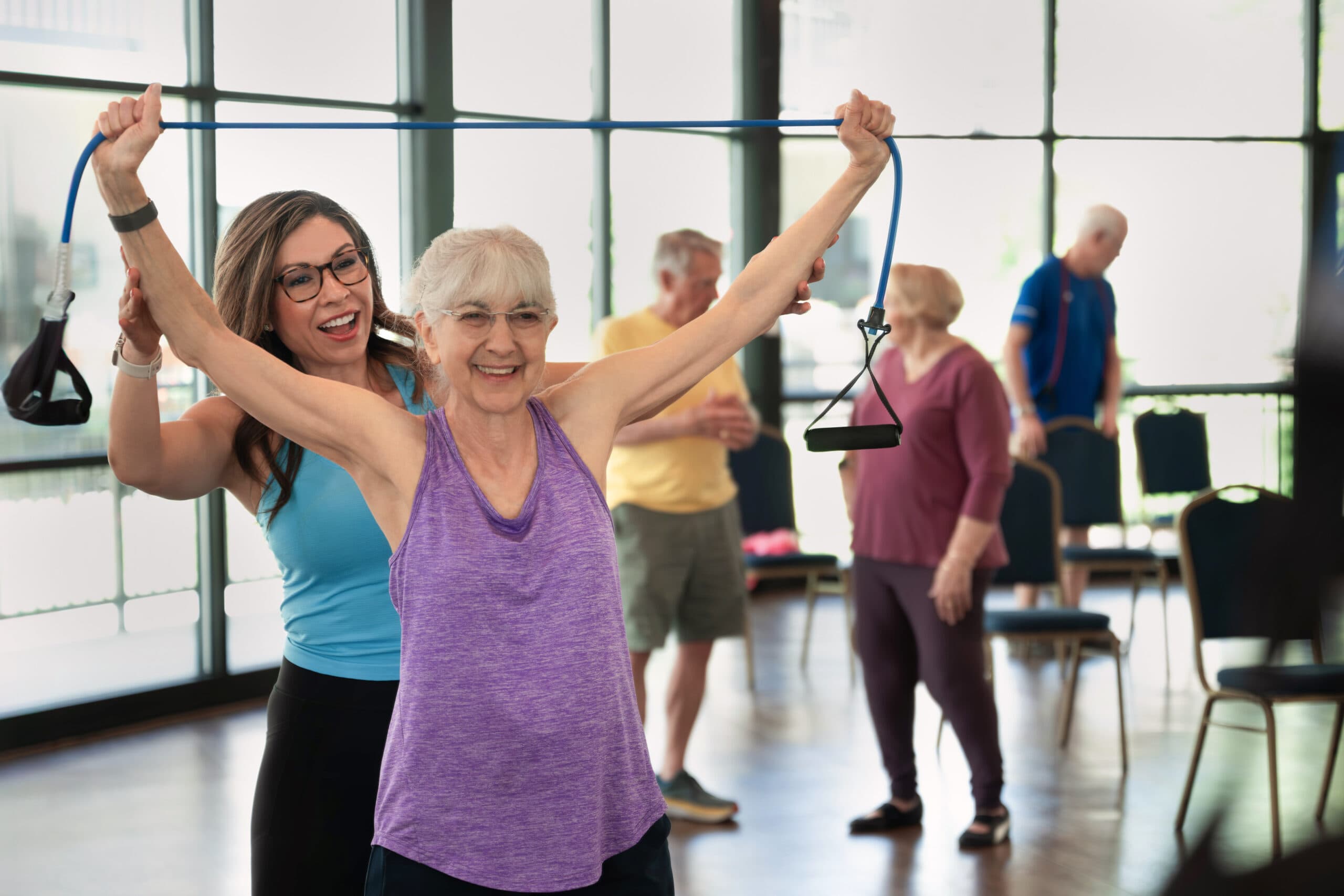 Two senior women seated next to a large orange exercise ball in a fitness studio, smiling towards the camera.